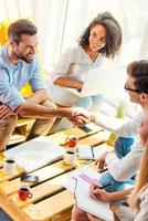 Welcome on board Two cheerful young men sitting at the wooden desk in office and shaking hands while two beautiful women looking at them and smiling photo