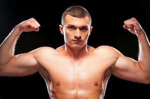 Strong man. Handsome young shirtless man looking up while standing against black background photo