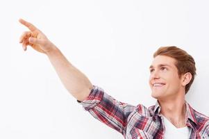 Look over there Handsome young man pointing away and smiling while standing against white background photo