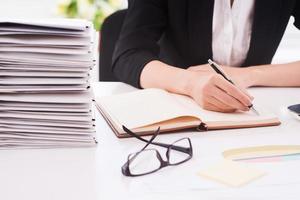 Doing office work. Cropped image of woman writing notes while sitting at her working place photo