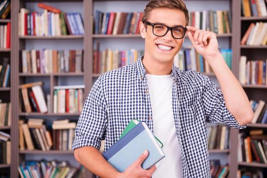 Student in library. Handsome young man holding books and smiling while standing in library photo