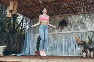 Full length of beautiful young woman in sports clothing using jumping rope on patio photo