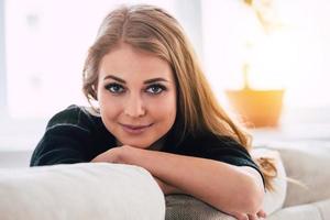 Magic look. Portrait of beautiful young woman looking at camera with smile while sitting on sofa at home photo