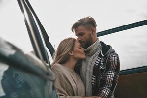 tan genial estar juntos. hermosa pareja joven abrazándose y sonriendo mientras está de pie al aire libre cerca de la mini furgoneta de estilo retro foto