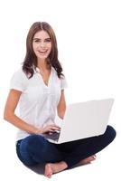 Having freedom to work everywhere . Beautiful young woman sitting on the floor and working on laptop against white background photo