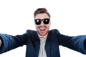 Capturing fun. Cheerful young man in shirt making selfie while standing against white background photo