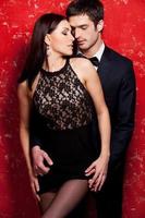 Unleashed desire. Beautiful young well-dressed couple bonding while standing against red background photo