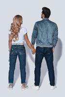 So great to be together. Full length rear view of young couple holding hands while standing against grey background photo