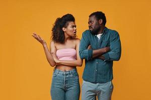 Young African couple gesturing and having conflict while standing against yellow background photo