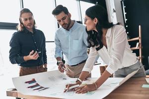 Best team ever. Group of young confident business people discussing something while woman working with blueprint in the office photo