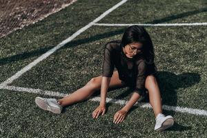naturalmente en forma y hermosa. mujer joven atractiva con ropa deportiva estirándose mientras se sienta en el campo de fútbol foto