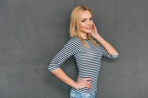 Elegant and gorgeous. Side view of beautiful young woman posing and looking at camera with smile while standing against grey background photo