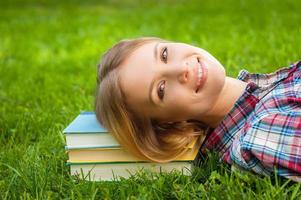 Taking break after studying. Beautiful young woman lying on the grass with head on the book stack photo
