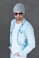 elegante guapo. apuesto joven en gafas y sombreros posando sobre fondo gris foto