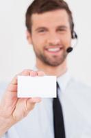 Call this number Handsome young man in formalwear and headset stretching out a business card and smiling while standing isolated on white background photo