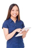 Woman with digital tablet. Cheerful young Asian woman using digital tablet and smiling while standing isolated on white photo