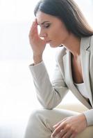 Depressed businesswoman. Side view of depressed young businesswoman in suit touching head with hand and keeping eyes closed while sitting at the chair photo