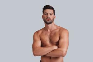 Masculinity and charisma. Handsome young man keeping arms crossed and looking at camera while standing against grey background photo