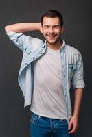 Candid and adorable. Cheerful young man looking at camera with smile while standing against grey background photo