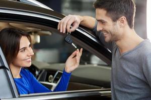 This car is yours Handsome young men standing near the car at the dealership and giving a key to his girlfriend sitting at the front seat photo