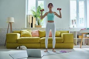 bella joven con ropa deportiva haciendo ejercicio con pesas en casa foto