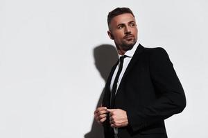 Ready to do business. Handsome young man in full suit adjusting jacket and looking away while standing against white background photo