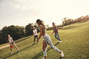 Summer activity. Group of young people in casual wear playing frisbee while spending carefree time outdoors photo
