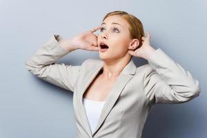 That is unbelievable Surprised young businesswoman holding head in hands and looking away while standing against grey background photo