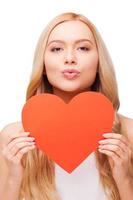 I love you Beautiful young blond hair woman holding big heart shaped valentine card and kissing you while standing isolated on white photo