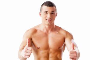 Join healthy lifestyle Cheerful young muscular man looking at camera and showing his thumbs up while standing against white background photo