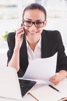 Confident businesswoman at work. Happy young woman in formalwear talking on the mobile phone while sitting at her working place photo