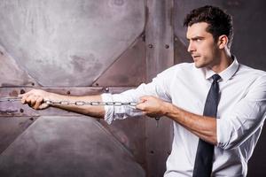 Everyday struggling. Side view of concentrated young man in shirt and tie stretching a chain photo