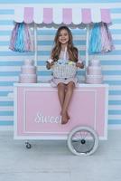 feliz por la pascua. linda niña sosteniendo huevos de pascua y sonriendo mientras se sienta en la decoración del carrito de dulces foto