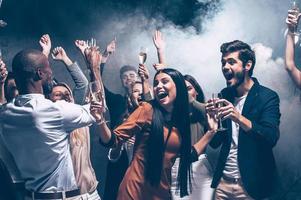 disfrutando de una fiesta increíble. grupo de hermosos jóvenes bailando con flautas de champán y luciendo felices foto