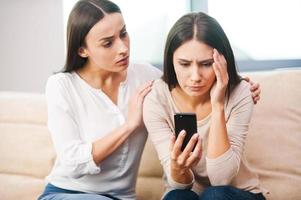 Real friends are always near. Depressed young woman holding mobile phone while being consoled by her friend photo
