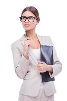 Thoughtful businesswoman. Confident young businesswoman holding clipboard and pen on chin while standing against white background photo