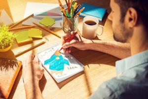 Just inspired. Close-up top view of man sketching on paper while sitting at his working place photo