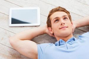 Thinking about solutions. Top view of handsome young man lying on the floor at his apartment while digital tablet lying near him photo