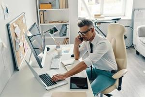 Smart and confident. Top view of good looking young man talking on the phone while sitting in the office photo