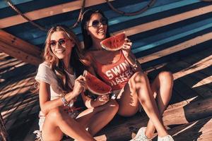 Enjoying summer refreshments. Top view of two attractive young women smiling and eating watermelon sitting outdoors photo