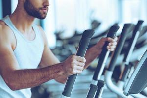 Working out. Side view close-up part of young man in sportswear working out on stepper at gym photo