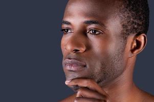 Thoughtful handsome. Young African man holding hand on chin while standing against black background photo