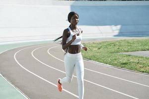 confiada joven africana en ropa deportiva corriendo en la pista al aire libre foto