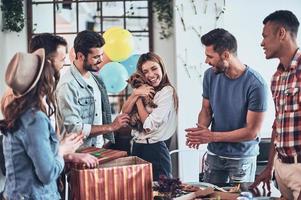 mejor regalo de cumpleaños. mujer joven feliz sosteniendo un cachorro y sonriendo mientras sus amigos están de pie alrededor foto