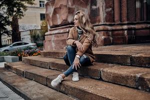 Always in style. Beautiful young woman looking away while sitting on stairs outdoors photo