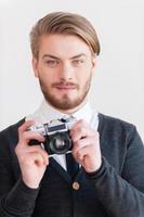 fotógrafo a la antigua. un joven guapo sosteniendo una cámara retro y sonriendo mientras se enfrenta a un fondo gris foto