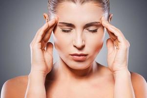 Awful headache. Mature shirtless woman holding head in hands and keeping eyes closed while standing against grey background photo