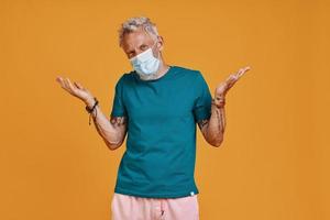 Senior man in protective facemask gesturing while standing against orange background photo