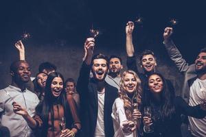 fiesta con amigos. Grupo de jóvenes alegres portando bengalas y copas de champán foto