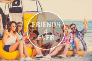 Friends forever. Group of happy young people having fun together while sitting on the beach near their retro van photo